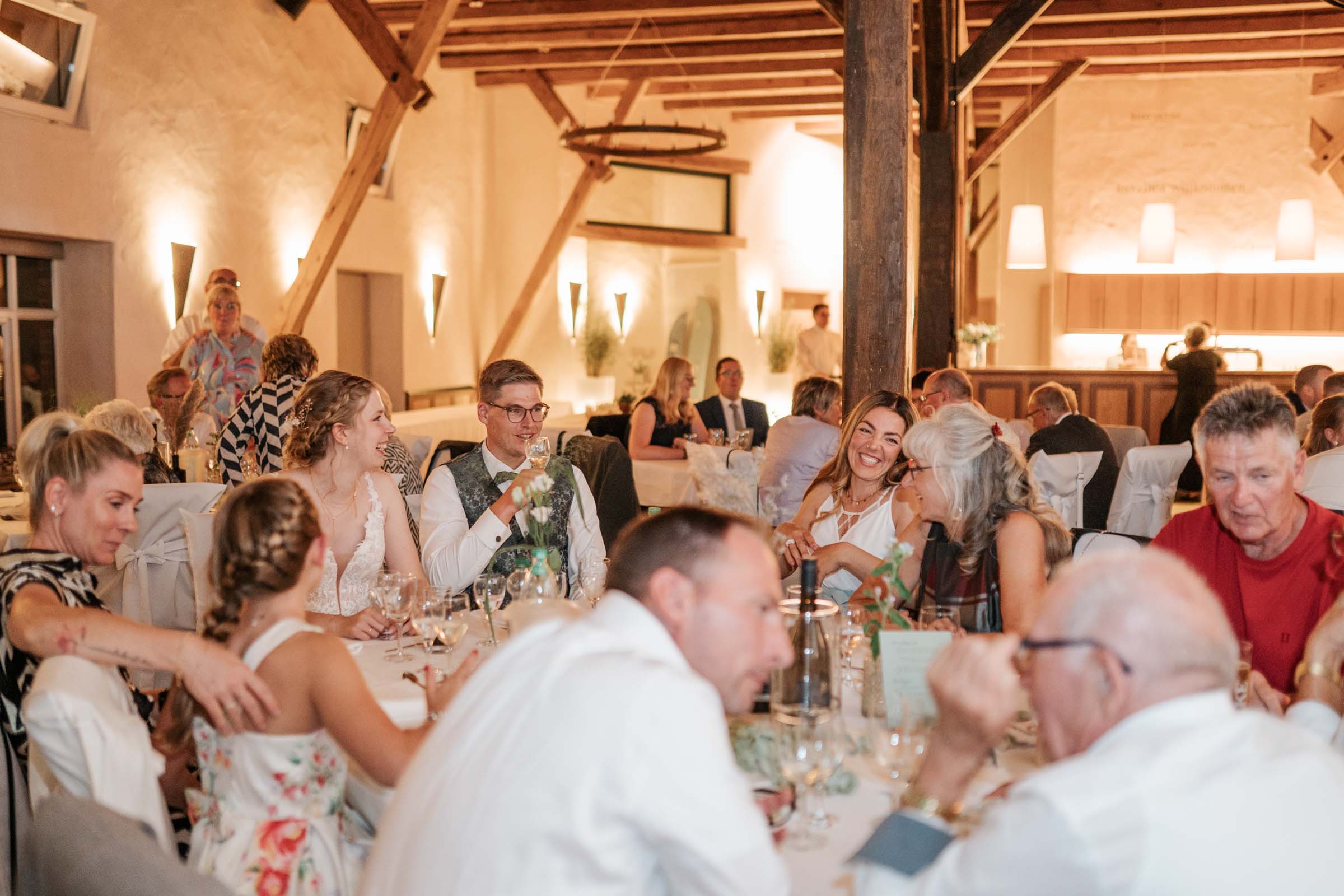 Brautpaar und Gäste unterhalten sich fröhlich am Tisch.