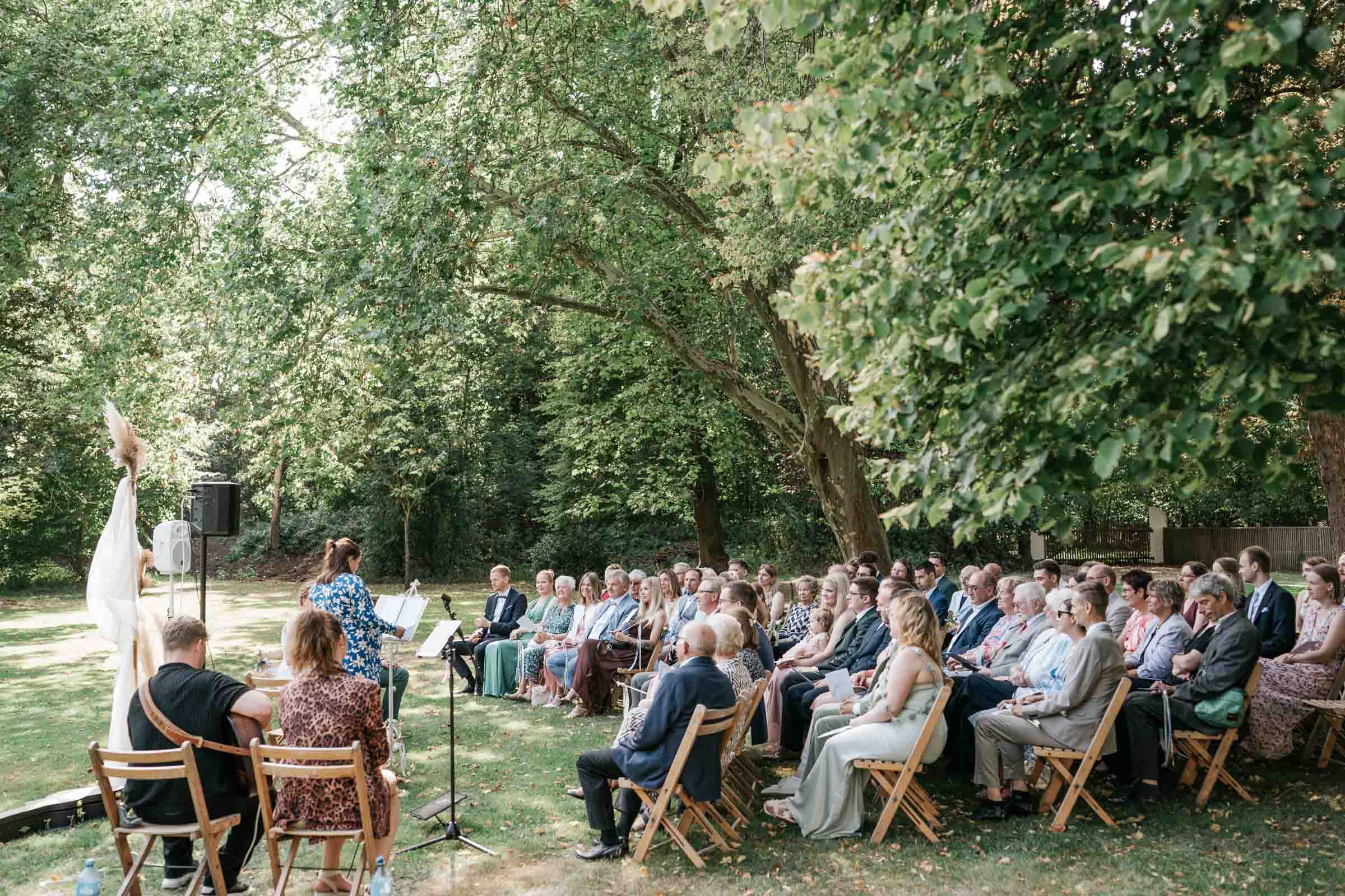 Sitzende Hochzeitsgäste im Park während der freien Trauung.