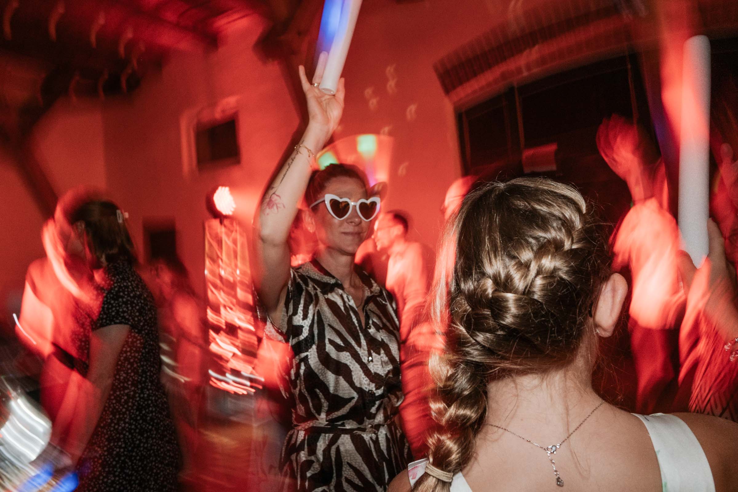 Gästin mit Herzbrille hebt LED-Schaumstoffstab auf der Tanzfläche.