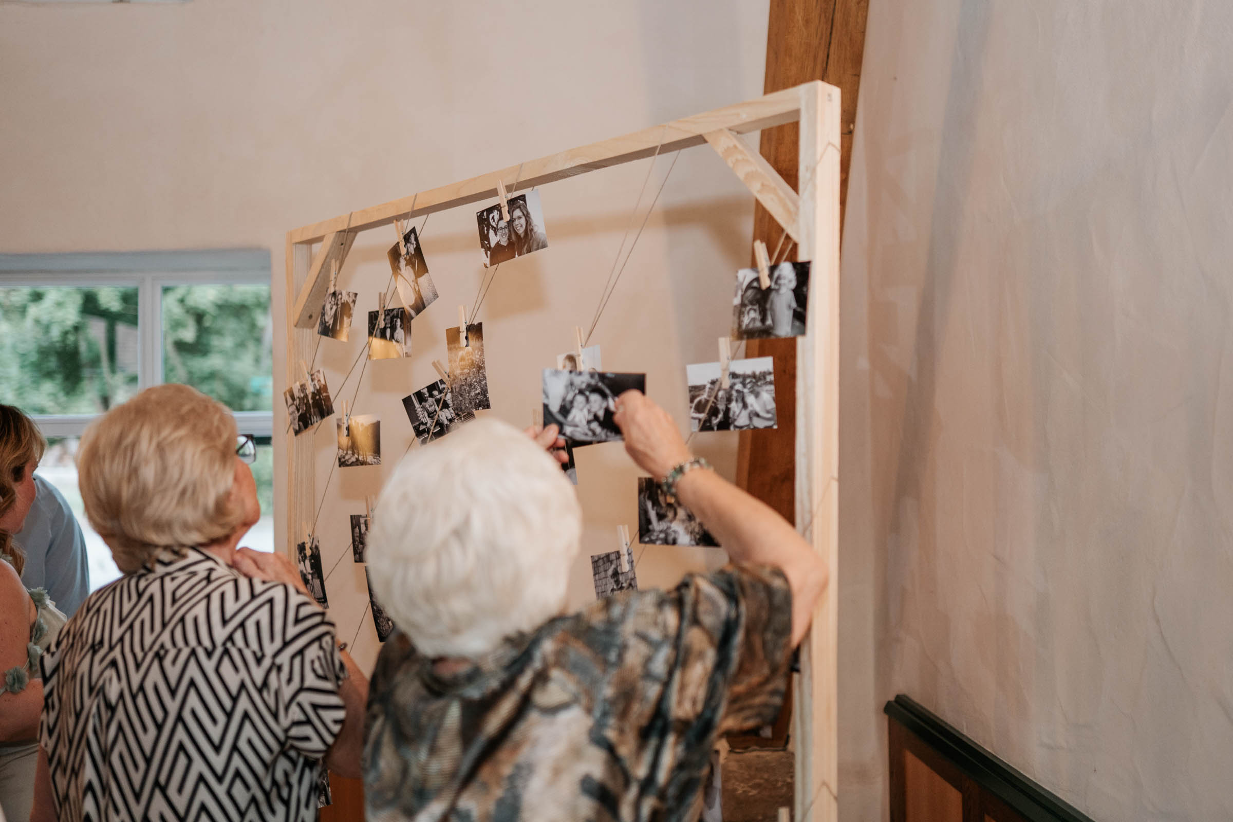 Fotowand mit aufgeklebten Erinnerungsfotos, Gäste hängen Bilder auf.