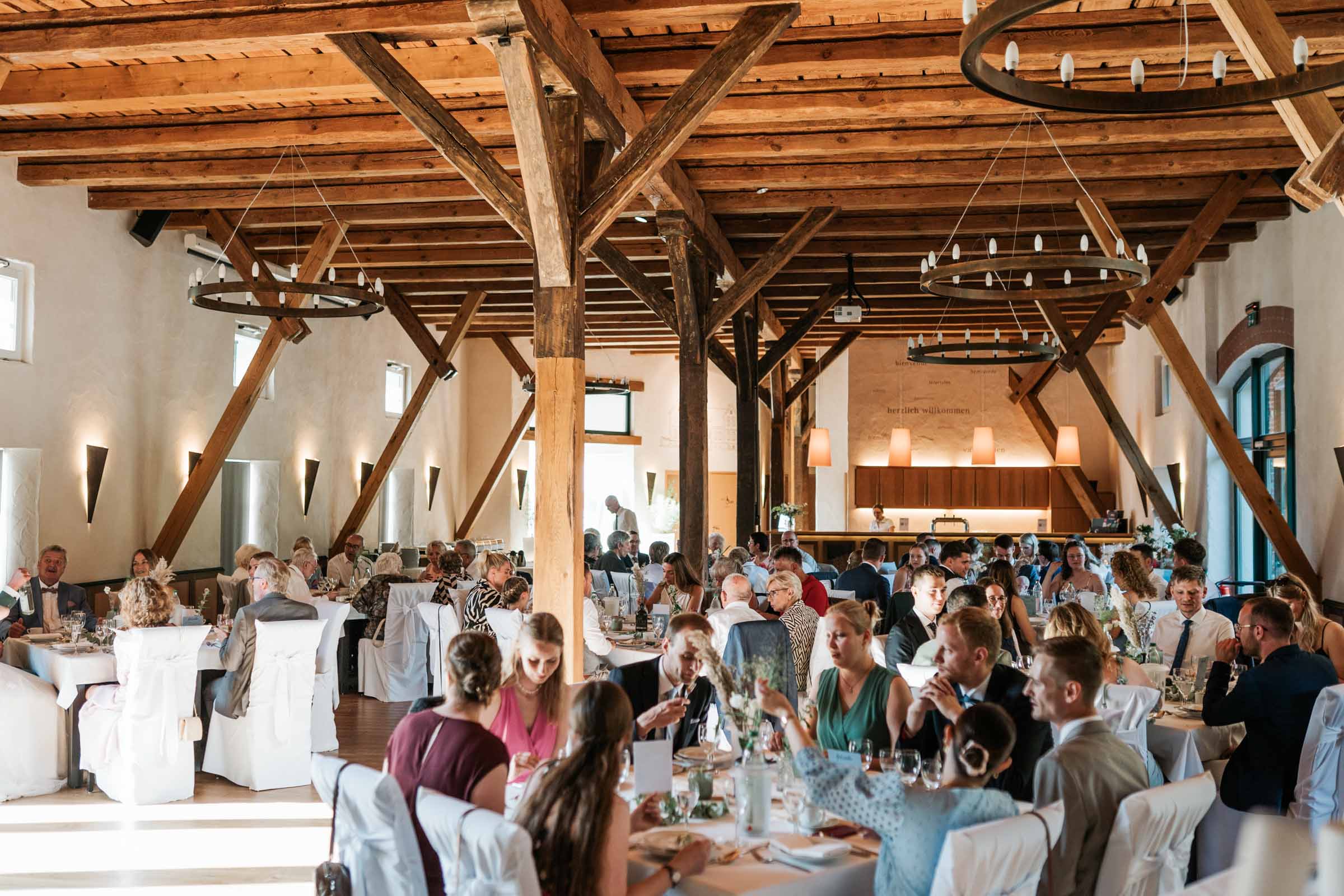 Großer Saal mit Holzbalken, runden Tischen und Ambientelicht.