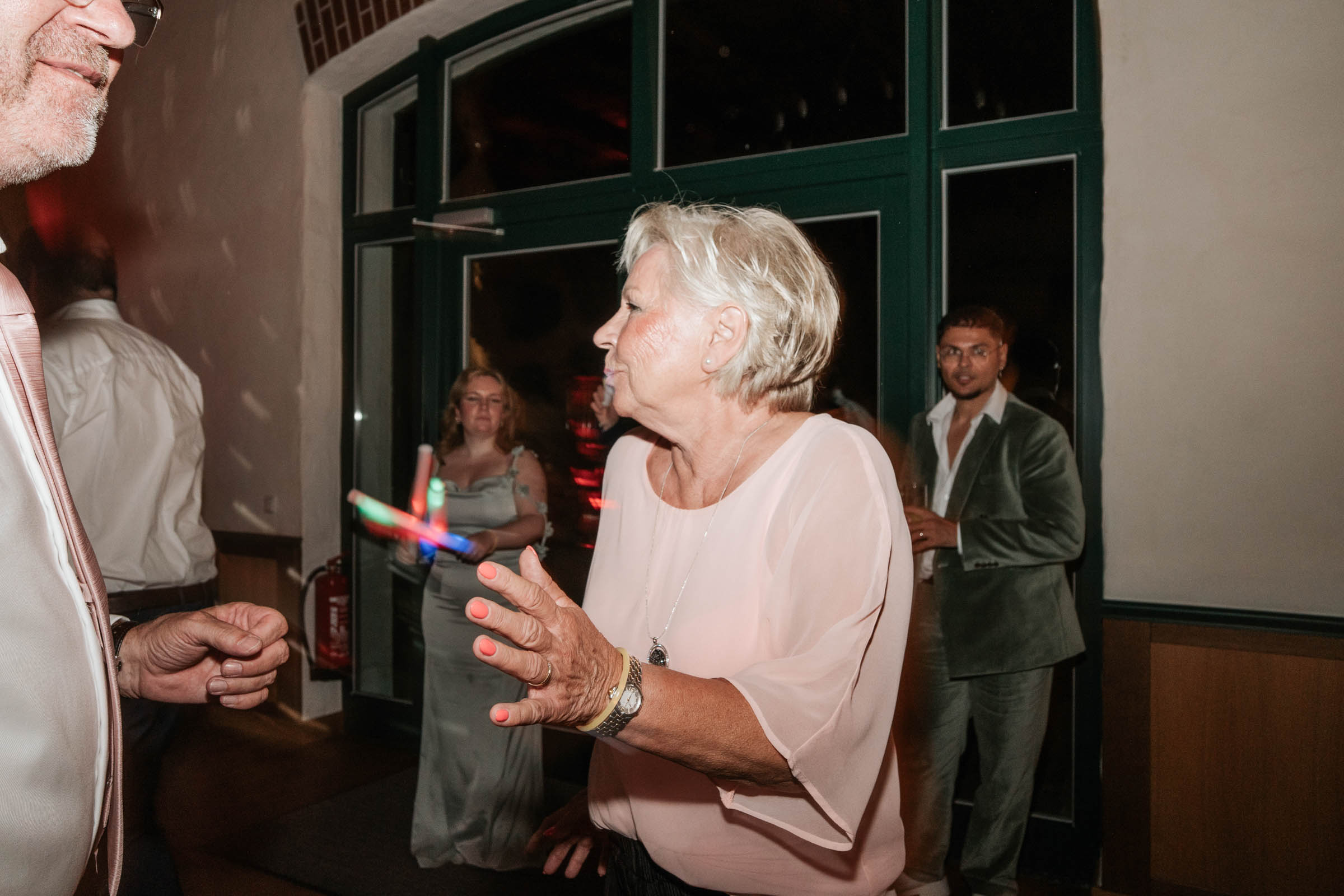 Gäste tanzen mit leuchtenden Sticks nahe des Saaleingangs.