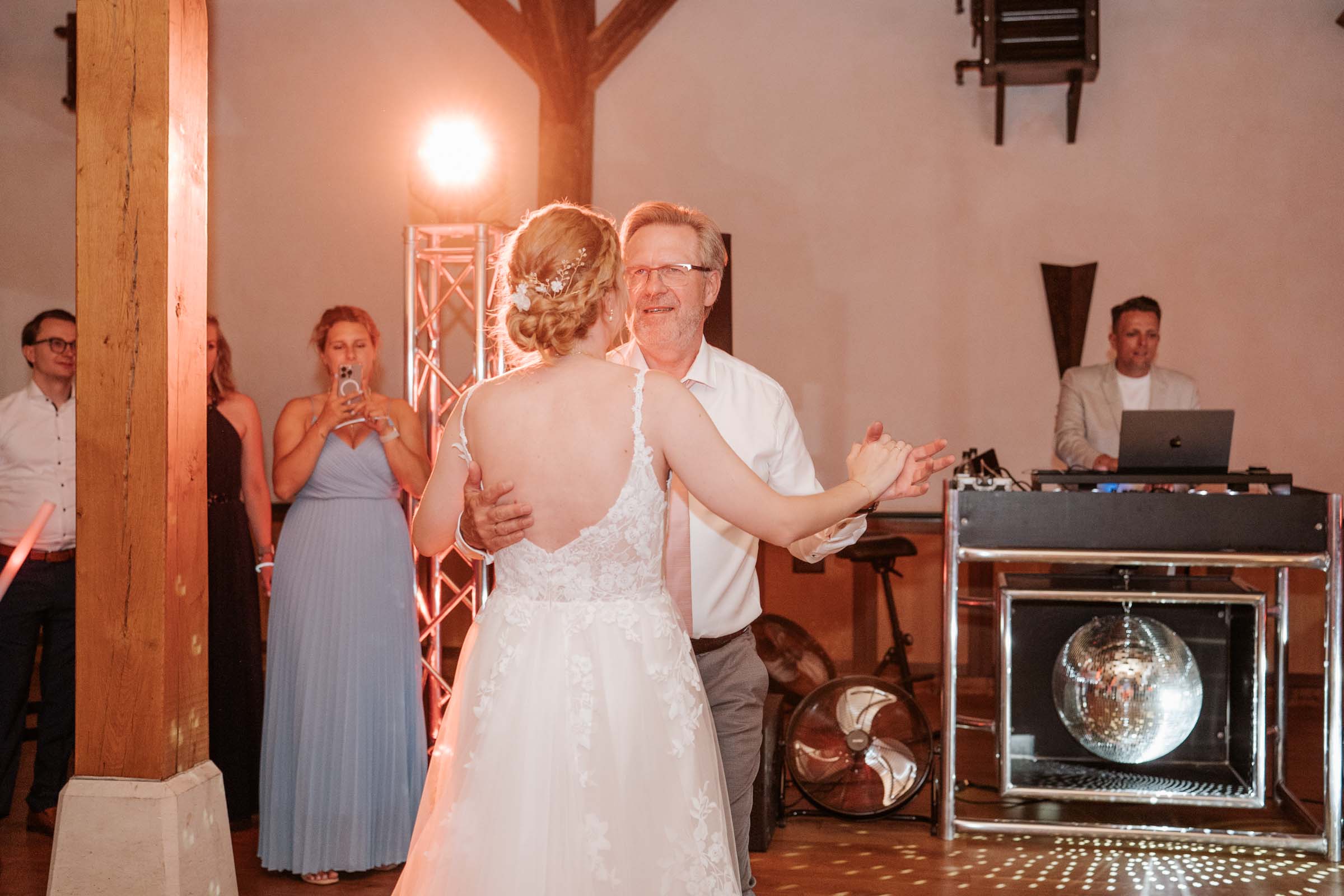 Vater tanzt mit der Braut; DJ-Pult und Discokugel im Hintergrund.