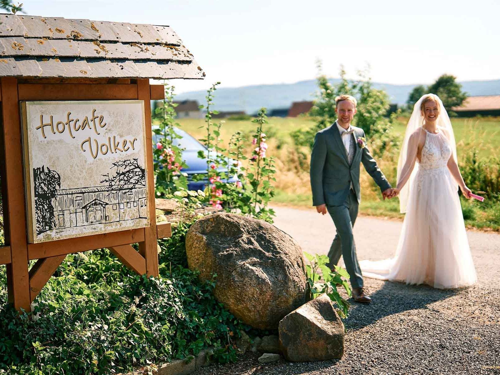 Brautpaar geht am Schild Hofcafé Volker vorbei.
